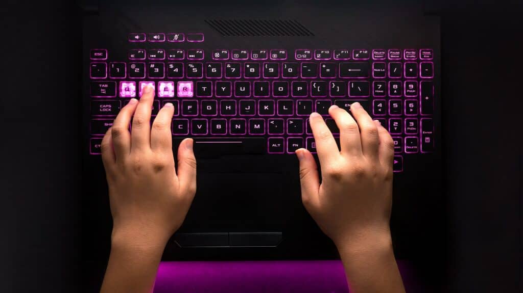 Hands typing on black gamer laptop with backlit keyboard