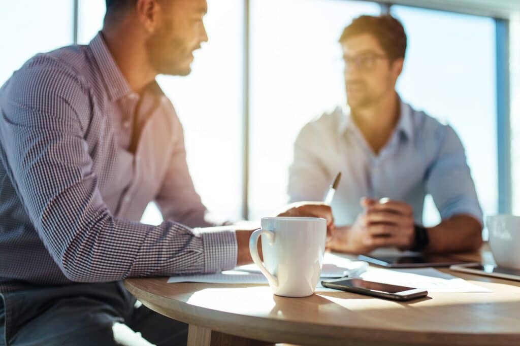 How to mentor a junior developer Business executives discussing work at office. Closeup of coffee cup with blurred image of two businessmen sitting on table.