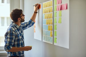 Young creative man writing down ideas on wall full of sticky notes