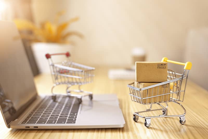 Brown paper boxs in a shopping cart with laptop keyboard on wood table in office background